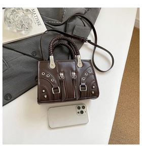 Detail of dark brown leather motorcycle bag with rivets, braided handle and smartphone