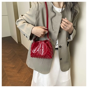 Dettaglio della texture con perle rosse su borsa a secchiello lucida con tracolla