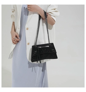 Detail of a black studded motorcycle bag with metal chain strap on a model's shoulder