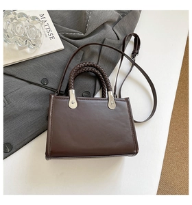 Detail of dark brown leather handbag featuring woven handles and silver metallic hardware