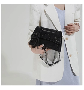 Detail of black leather handbag with silver studs and chain strap on female model