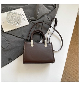 Detail of a brown PU leather handbag with woven handles and silver metal hardware