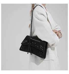 Detail of black punk shoulder bag with silver rivets and metal chain on white blazer