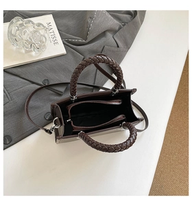 Detail view of brown leather bag with braided handles and triple interior compartments