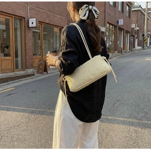 Chic beige baguette bag with star print and side bow ribbon shown on a shoulder