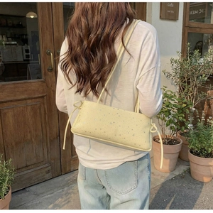 Detail of light yellow baguette bag with star patterns worn by a woman in a cafe setting