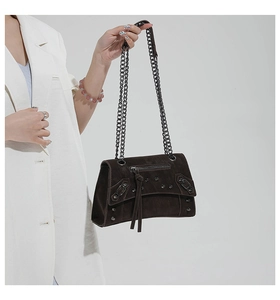 Detail of dark brown suede crossbody bag with vintage rivets and metal chain strap