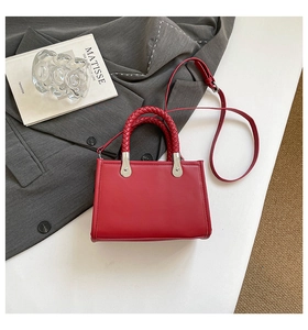 Close-up of red leather handbag with woven handles and silver buckles on a suit jacket
