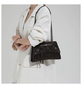 Model wearing dark brown studded motorcycle bag with chain strap and tassels