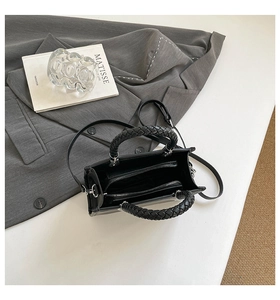 Macro view of black leather handbag featuring woven handles and internal zip compartments