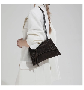 Detail of dark brown suede crossbody bag with metal rivets, chain strap and fringe