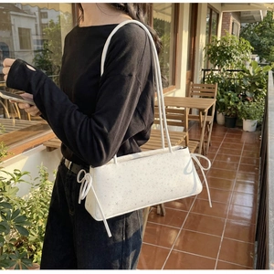 Detailed side view of white shoulder bag with silver star prints and ribbon bow accents