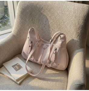 Détail d'un sac hobo rose clair avec clous argentés et détails métalliques sur un canapé