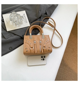 Detail of light brown handbag with woven handles and metal zippers next to a smartphone