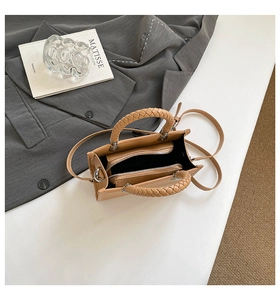 Detail view of khaki handbag featuring woven handles and dual zipper compartments