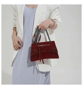 Detail of burgundy suede crossbody bag with metallic rivets and classic chain strap