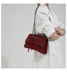 Detail of red suede crossbody bag with silver rivets and metal chain on white blazer