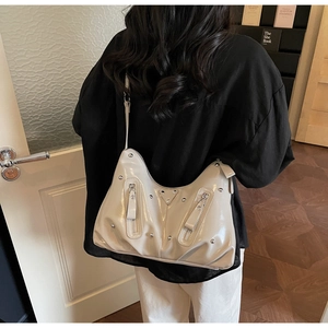 Détail du sac hobo en cuir verni crème avec rivets argentés et plaque de logo