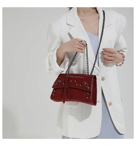 Detail shot of a dark red motorcycle crossbody bag with rivets and chain strap on a model