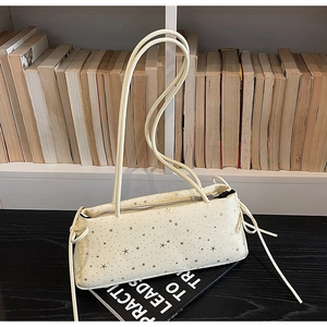 Detail of cream baguette bag with silver star prints resting on books in a cozy setting