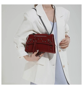 Deep red studded leather shoulder bag worn over a white blazer for a chic biker look