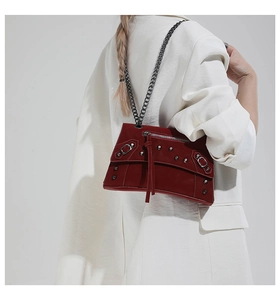 Detail of red suede crossbody bag with silver studs and chain strap on white blazer