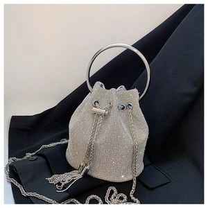 Detail of silver rhinestone bucket bag with metal handle and drawstring tassels on dark suit
