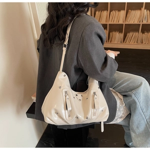 Détail d'un sac hobo crème avec clous argentés et fermetures éclair latérales sur mannequin