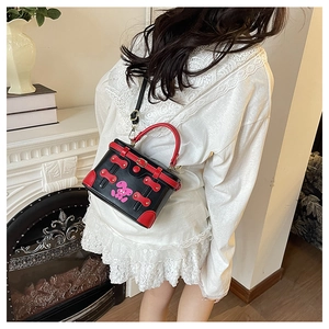 Detail of creative black and red box bag with pink rabbit worn as a crossbody bag