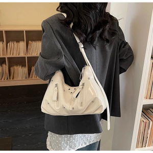 Détail du sac hobo en cuir verni blanc avec rivets argentés et fermetures éclair dans un bureau