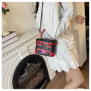 Close-up of black box bag featuring red leather trim and cartoon graphic detail