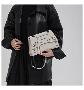Detail of oatmeal leather crossbody bag featuring silver rivets and chain strap accents