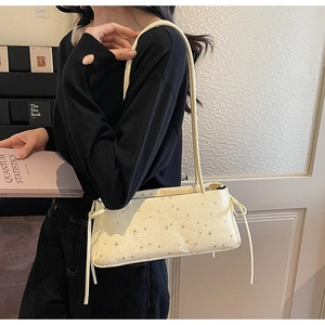 Detail of cream shoulder bag with silver star patterns and drawstring bow on model