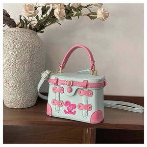 Detail of mint green box bag with pink rabbit print and golden buckle on wood shelf