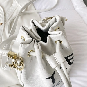 Detail of white lychee leather bucket bag featuring gold hardware and black letter print