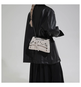 Detail of studded motorcycle style crossbody bag with metal chains on a model
