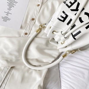 Close-up of white lychee leather bucket bag with bold letters and gold hardware