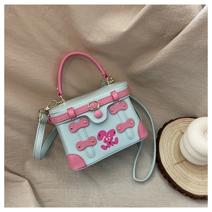 Detail of light blue box bag with pink handles and cartoon rabbit motif on beige fabric