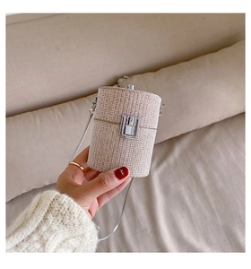 Detail of beige woven mini cylinder bag with silver metal buckle and chain strap