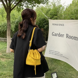 Detail of yellow pebbled leather bucket bag featuring drawstring and THE BUCKET print