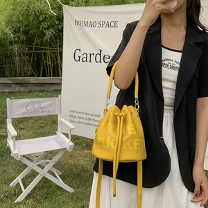 Close-up of bright yellow drawstring bucket bag with THE BUCKET print and golden hardware