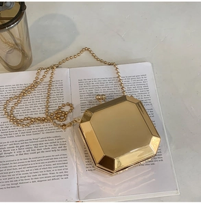 Detail of a polished gold octagonal clutch bag with a bead chain on an open book