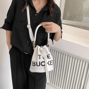 Detail of white leather bucket bag with The Bucket lettering and gold metal hardware
