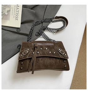 Detail of dark brown suede crossbody bag with silver rivets and metal chain strap