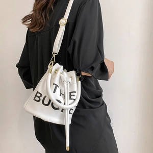 Detail of white lychee-grain bucket bag featuring black text and golden hardware