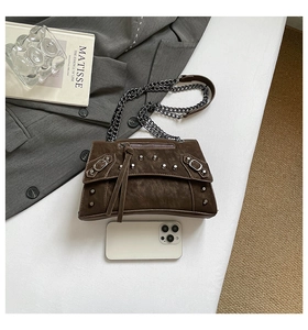 Close-up of vintage brown leather bag with rivets, tassels and silver chain strap details