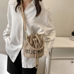 Chic beige pebbled leather bucket bag with THE BUCKET letter print and adjustable strap