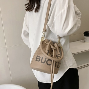 Detail of a khaki leather bucket bag with THE BUCKET print and drawstring closure