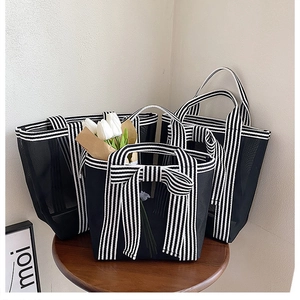 Detail view of a three-piece black mesh tote bag set with striped handles and bow decoration