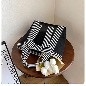 Detail of minimalist mesh tote bag with striped straps on a rustic table with flowers